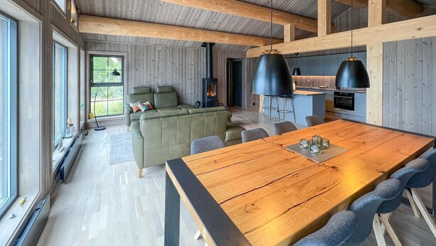 A modern interior with a wooden dining table, green sofa, and a kitchen area with a stove. - Lovely home in Gålå with sauna (Gålå)