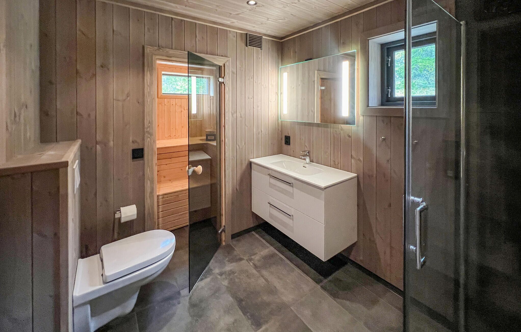 A compact bathroom with a wooden interior, a glass shower enclosure, and a white sink.