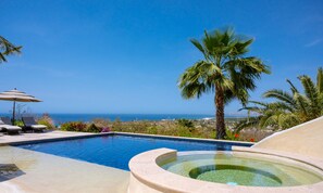 Une piscine avec un jacuzzi, des chaises longues et une vue sur l’océan.