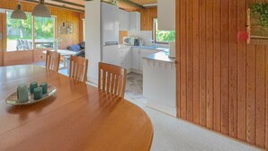 A modern kitchen with white cabinets, a dining area with a wooden table and chairs, and a view of the outdoors through large windows.