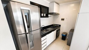 A modern kitchen with stainless steel appliances, a black countertop, and white cabinetry. - Hosts BR - Flat frente mar (Fortaleza)