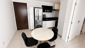 A modern kitchen with white cabinets, a stainless steel refrigerator, and a black countertop. - Hosts BR - Flat frente mar (Fortaleza)