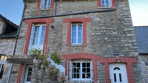 A stone building with red brick accents, numbered 7, featuring a central entrance with a white door and a small balcony above.
