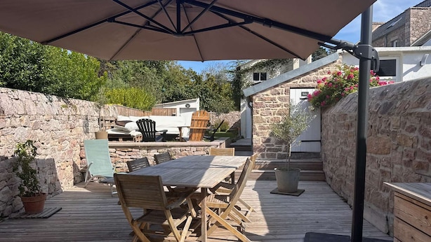 An outdoor patio with a wooden table and chairs, a large umbrella, and stone walls.