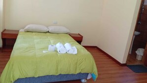 Quarto de hotel com uma cama, almofadas, mesa de cabeceira de madeira e uma pequena mesa.