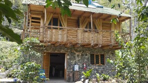 Uma cabana de madeira com dois andares, fachada de pedra, varanda e entrada em pedra.