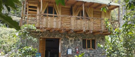 A two-story wooden cabin with a stone facade, a balcony, and a stone entrance.