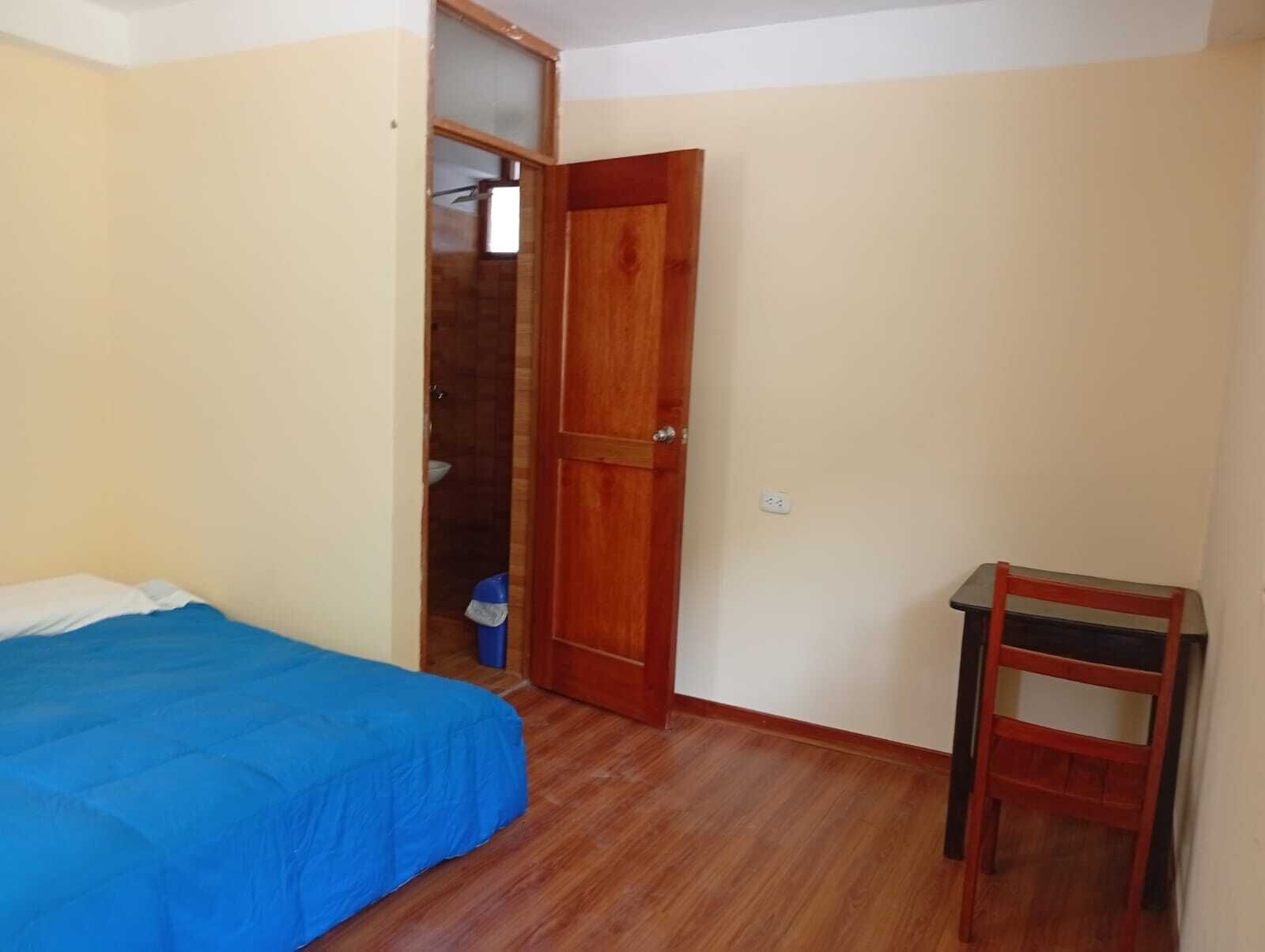 Un dormitorio con cama, una puerta de madera, una silla y un armario pequeño.