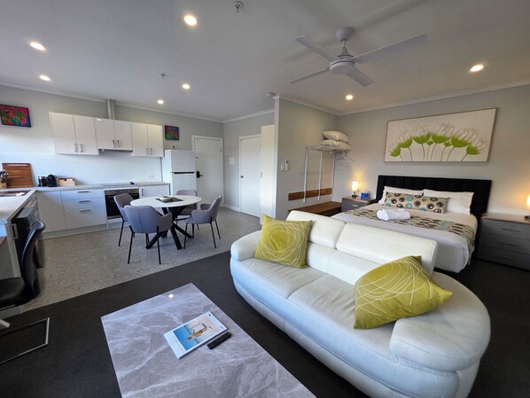 Quarto de hotel moderno com cama, sofá, área de refeições e cozinha.