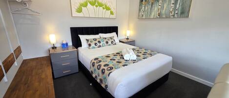A neatly made bed with a patterned bedspread, a bedside lamp, and a wall-mounted painting.