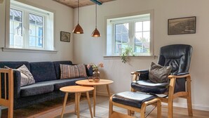 Ett vardagsrum med en mörkblå soffa, en trästol, ett litet runt bord och ett stort fönster med utsikt över hus.