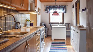 A compact kitchen with wooden cabinets, a tiled backsplash, a central island, and a striped rug. - 3 bedroom awesome home in Sölvesborg (Sölvesborg)