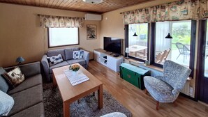 A cozy living room with a sofa, a coffee table with a vase, a TV, and a window with curtains. - 3 bedroom awesome home in Sölvesborg (Sölvesborg)