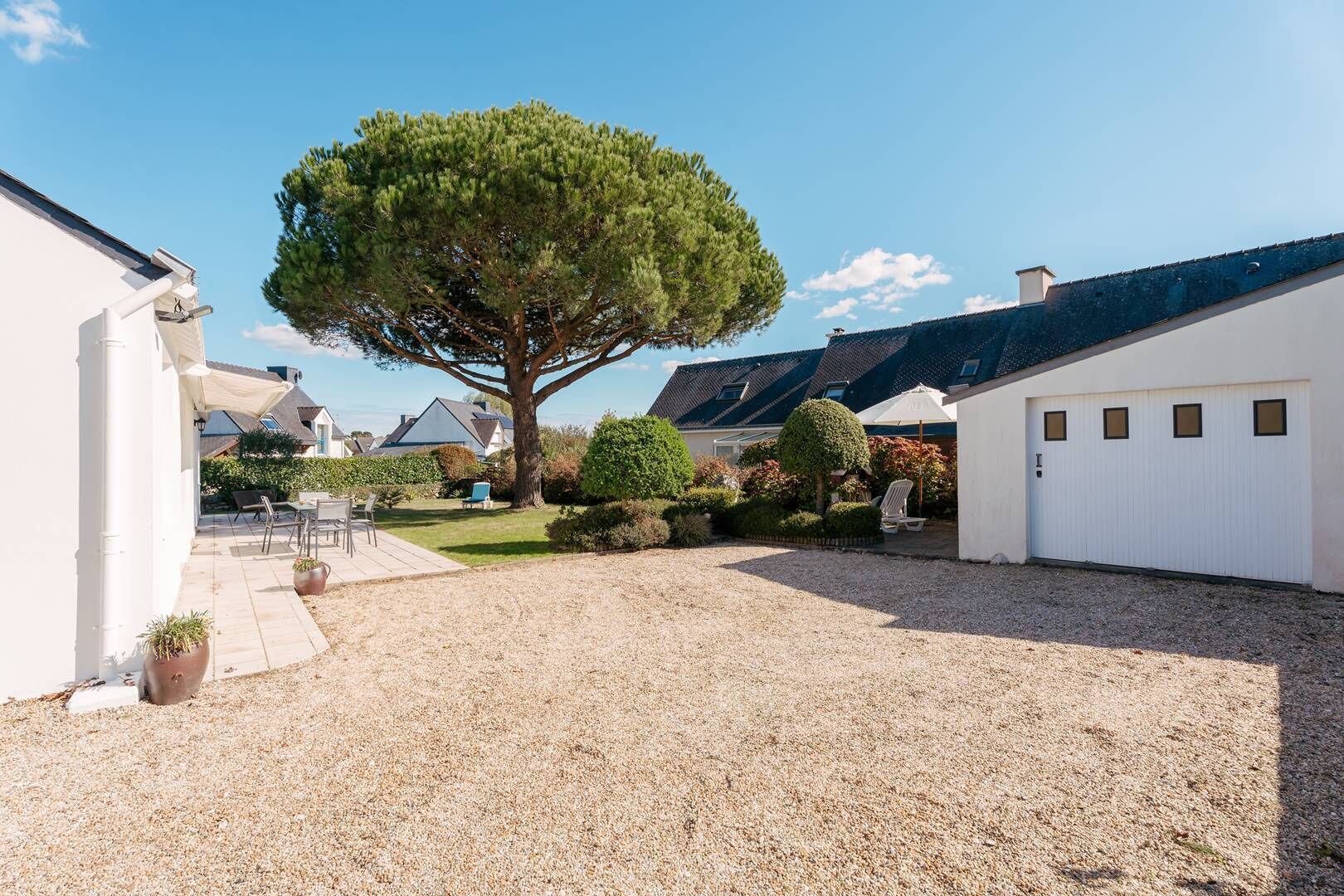 Propiedad residencial con camino de entrada de grava, un árbol grande y un garaje blanco.