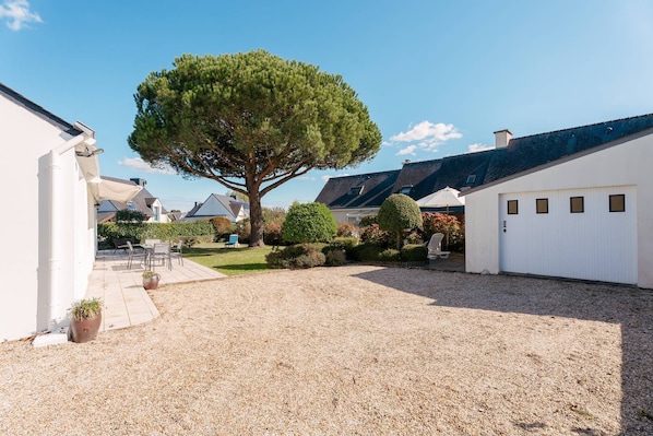 A residential property with a gravel driveway, a large tree, and a white garage.