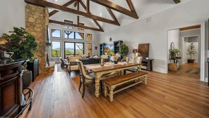 Un comedor espacioso con una mesa de madera y bancos, rodeado de paredes de piedra y grandes ventanas que ofrecen vistas al exterior.