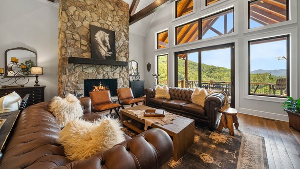 Un salón espacioso con chimenea de piedra, sofás de cuero y grandes ventanales con vistas al exterior.
