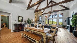 Un salón comedor espacioso con mesa de madera, asientos cómodos, chimenea de piedra y ventanas amplias con vistas al exterior.