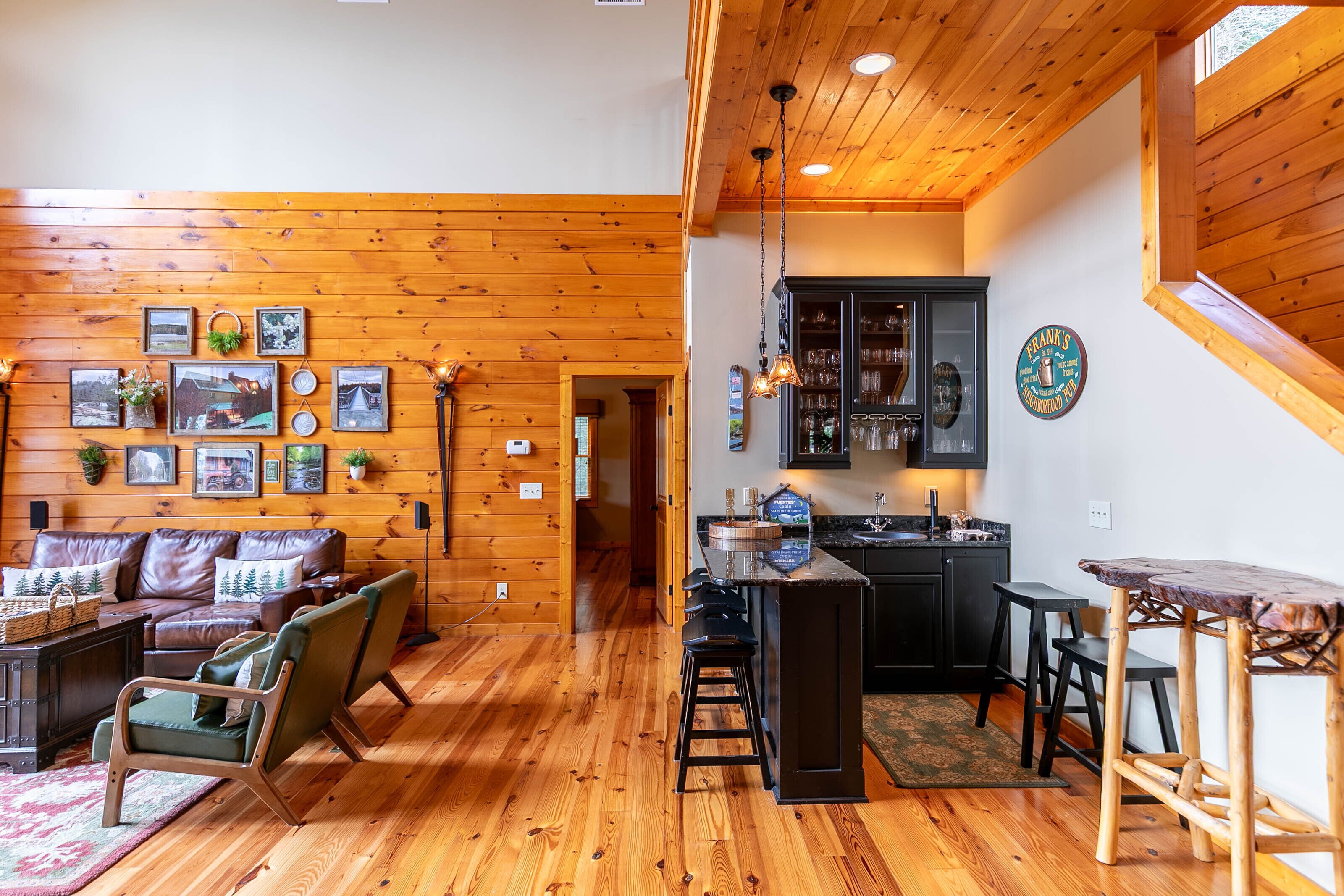Een gezellig cabin interieur met houten vloer, een zithoek met een bank en fauteuils, een keuken met barkrukken en een eettafel.