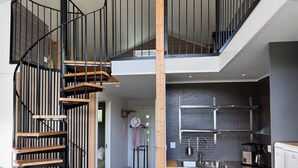 A modern interior with a spiral staircase, a kitchen with dark tiles, and a visible bed in the adjacent room.