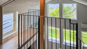 A staircase with a black railing, wooden posts, and a view of a green lawn and houses through large windows.