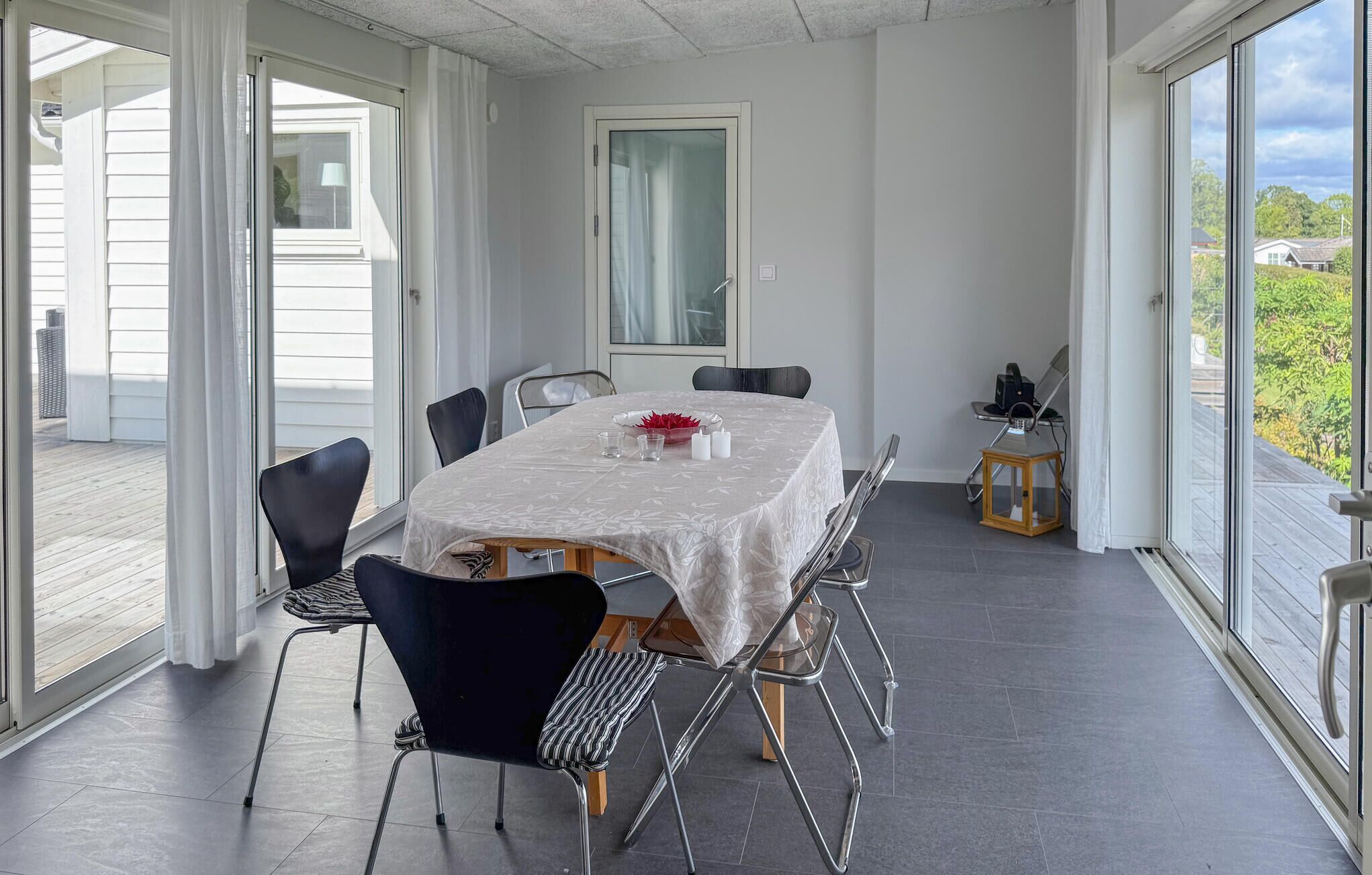 Een eetgedeelte met een tafel voor vier personen, omringd door stoelen en grote ramen met uitzicht op groen.