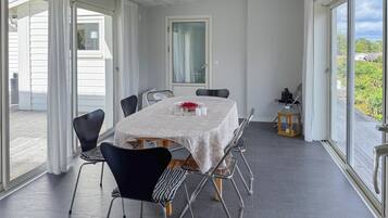Een eetgedeelte met een tafel voor vier personen, omringd door stoelen en grote ramen met uitzicht op groen.