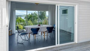 A covered outdoor dining area with a table and chairs, a view of greenery and a body of water, and a sliding glass door.