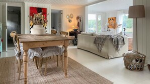 A spacious living room with a wooden dining table, a sofa, and a large window providing natural light. - Beautiful home in Säffle with lake view (Säffle)