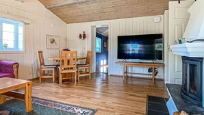 Un soggiorno con pavimento in legno, televisione, camino e zona pranzo con sedie e tavolo.