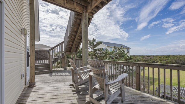 Une terrasse en bois avec des fauteuils Adirondack, un escalier en bois et une vue sur une maison et le paysage environnant.