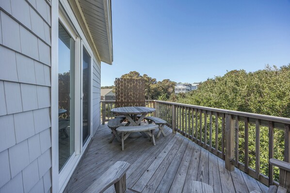 A wooden deck with a table and benches, a railing, and a view of trees and buildings in the background.