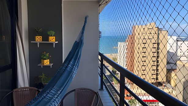 Un balcón con una hamaca, una silla y vistas a edificios a través de una cerca de malla.