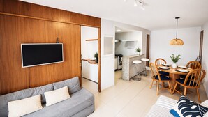 Una sala de estar moderna con un sofá gris, un televisor de pantalla plana y un comedor con sillas de madera y una mesa.