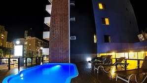 Una piscina con cubierta de madera, pared de ladrillo y mobiliario exterior.