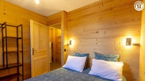 A wooden room with a bed, two pillows, a ladder, and wall-mounted lights. - RESIDENCE ORIONDE - L'OURSON (LES DESERTS)