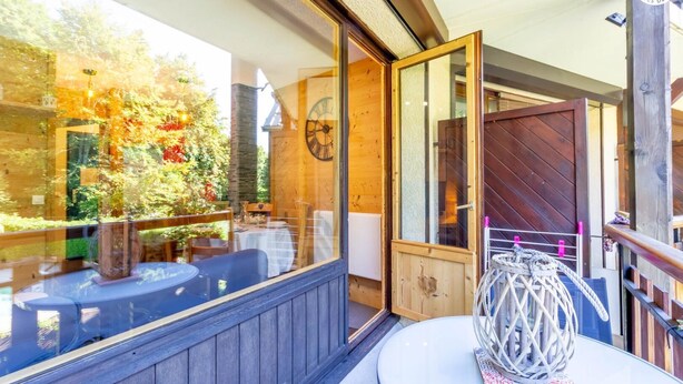 A wooden deck with outdoor seating, a glass balustrade, and a decorative rope sculpture on a table. - RESIDENCE ORIONDE - L'OURSON (LES DESERTS)