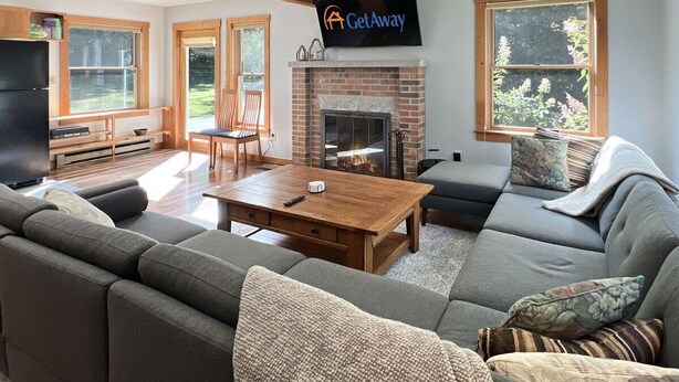 A modern living room with a fireplace, a large sectional sofa, a wooden coffee table, and a flat-screen TV mounted on the wall.