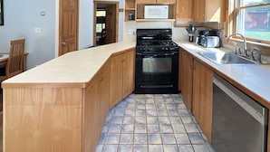 A compact kitchen with wooden cabinets, a black stove, a microwave, and a dishwasher.