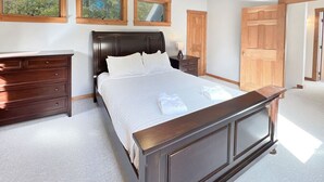 A bedroom with a large bed, wooden nightstands, a ceiling fan, and wooden doors. - Hidden Kingdom | Near Echo Lake, Private Retreat w/ Outdoor Space (Plymouth)