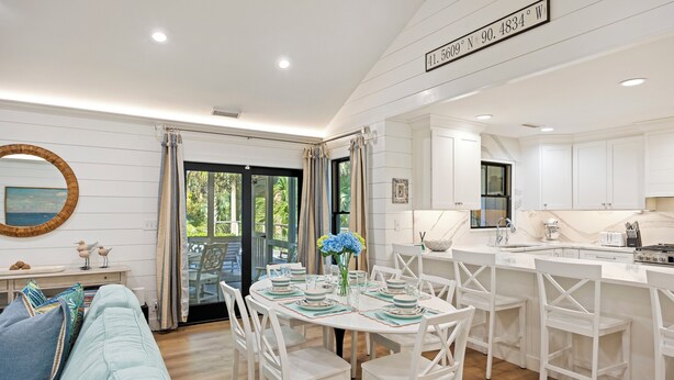A modern kitchen with white cabinetry, a dining area with white chairs, and a large window with curtains. - KIAWAH, West Beach, 5BR Luxury Home, POOL & Incredible PORCHES! (Kiawah Island)