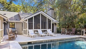 A poolside area with a covered seating area, lounge chairs, and a barbecue grill. - KIAWAH, West Beach, 5BR Luxury Home, POOL & Incredible PORCHES! (Kiawah Island)