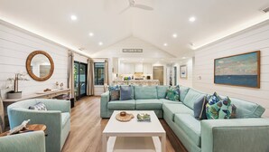 A spacious living room with a teal sectional sofa, a white coffee table, and a ceiling fan. - KIAWAH, West Beach, 5BR Luxury Home, POOL & Incredible PORCHES! (Kiawah Island)