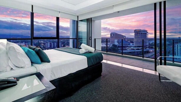 Una camera d'albergo moderna con un letto grande, una scrivania e vista sulla città attraverso ampie vetrate.
