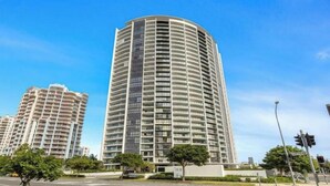 Un edificio residenziale a grattacielo con facciata curva, numerosi balconi e un cielo azzurro sullo sfondo.