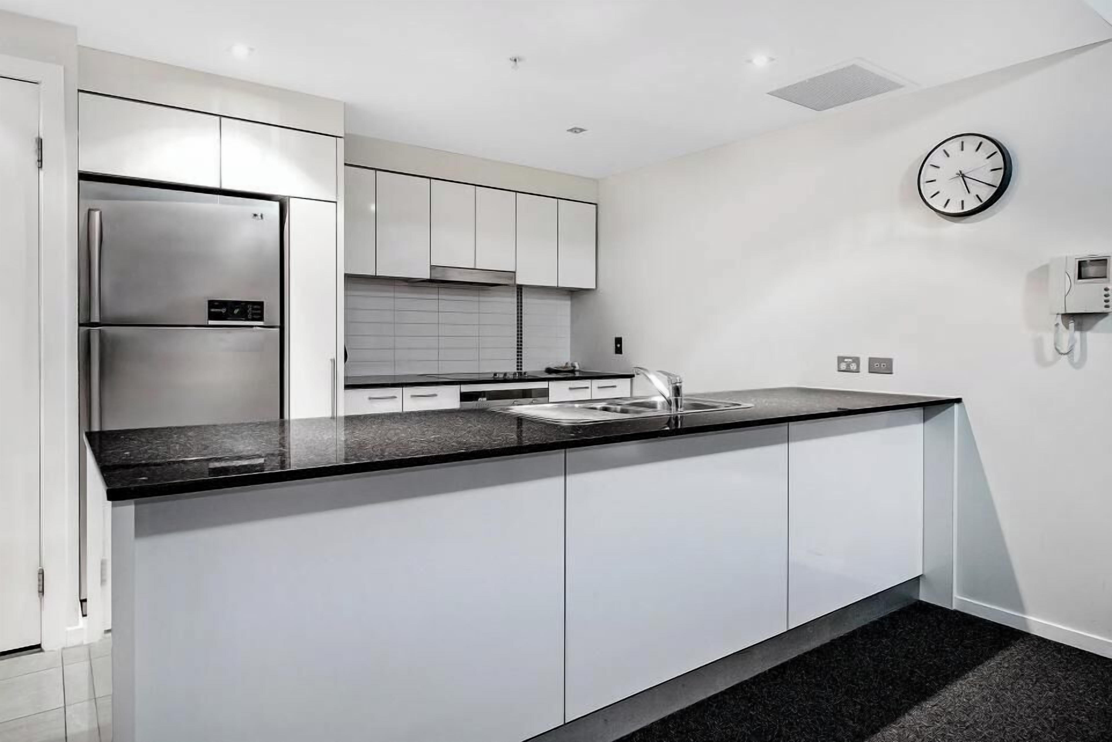 A modern kitchen with white cabinetry, a stainless steel refrigerator, a black countertop, and a wall-mounted clock.