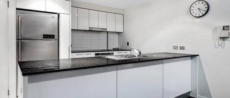 A modern kitchen with white cabinetry, a stainless steel refrigerator, a black countertop, and a wall-mounted clock.