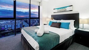 Una camera d'hotel moderna con un grande letto e vista sulla città attraverso ampie finestre a tutta altezza, con uno skyline urbano visibile.