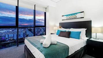 A modern hotel room with a large bed, a city view through floor-to-ceiling windows, and a cityscape visible outside.