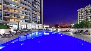 Una piscina con lettini, circondata da edifici moderni con balconi e finestre.